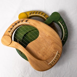 May include: Two wooden lyres, one green and one yellow, with strings and tuning pegs. The lyres are made of wood and have a natural finish.