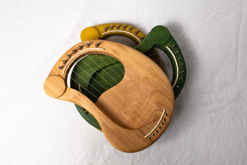 May include: Two wooden lyres, one green and one yellow, with strings and tuning pegs. The lyres are made of wood and have a natural finish.