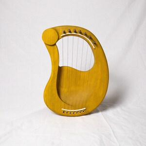 May include: A yellow wooden lyre with strings and a sound hole. The lyre is a musical instrument.