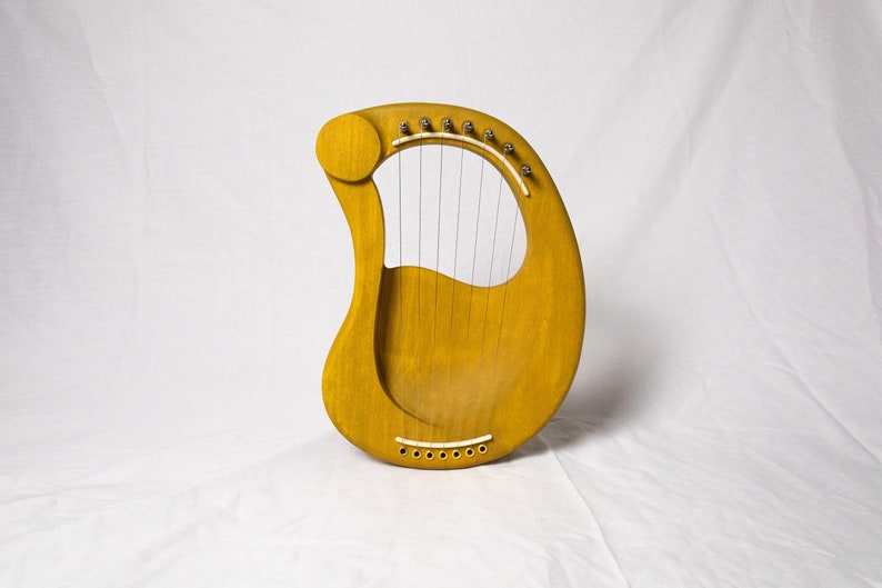 May include: A yellow wooden lyre with strings and a sound hole. The lyre is a musical instrument.