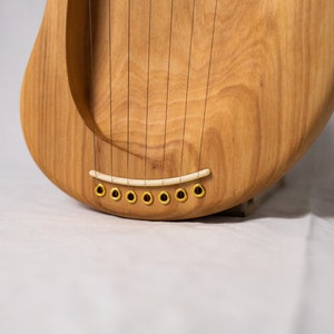May include: Close-up of a wooden lyre with a white bridge and gold tuning pegs.