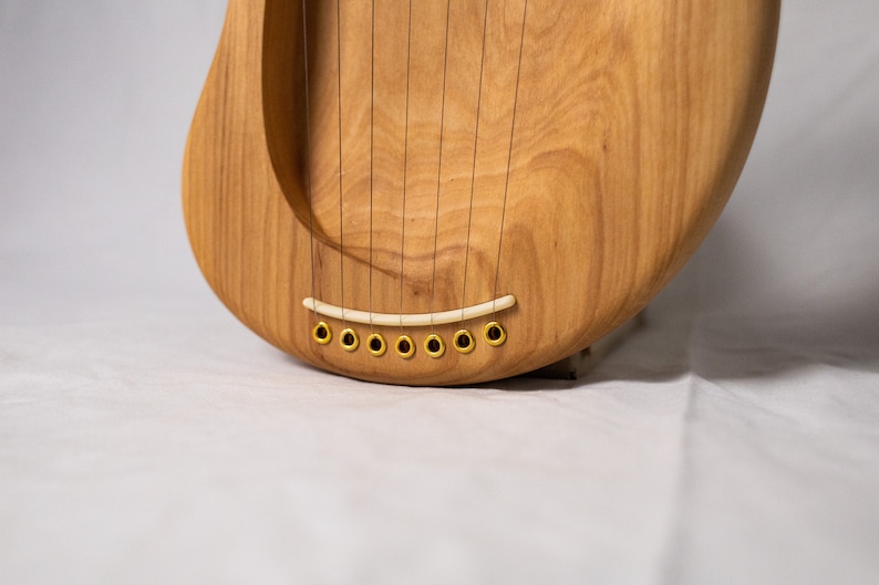 May include: Close-up of a wooden lyre with a white bridge and gold tuning pegs.