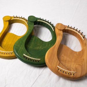 May include: Three wooden lyres, one yellow, one green, and one natural wood color. Each lyre has strings and a curved shape.