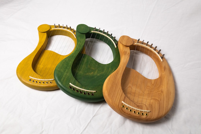 May include: Three wooden lyres, one yellow, one green, and one natural wood color. Each lyre has strings and a curved shape.