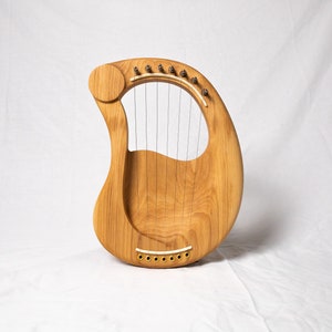 May include: A wooden lyre with a natural finish and strings. The lyre has a rounded shape and a small sound hole.