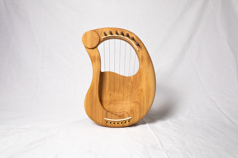May include: A wooden lyre with a natural finish and strings. The lyre has a rounded shape and a small sound hole.