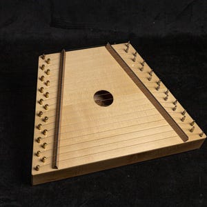 May include: A wooden dulcimer with a triangular shape and a sound hole in the center. The dulcimer has strings and brass tuning pegs.