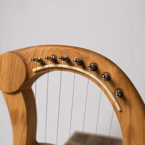 May include: A wooden lyre with a natural wood finish and chrome tuning pegs. The lyre has a white string guide and multiple strings.