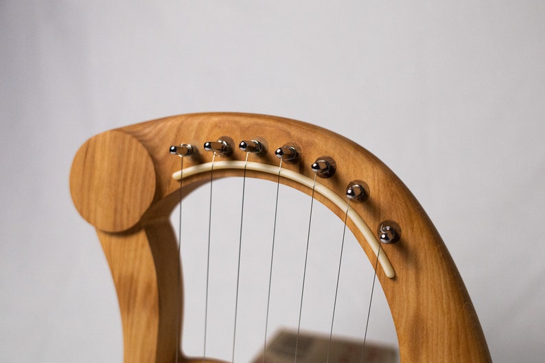 May include: A wooden lyre with a natural wood finish and chrome tuning pegs. The lyre has a white string guide and multiple strings.
