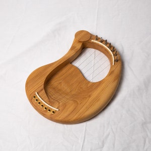 May include: A wooden lyre with a natural wood finish and a light brown color. The lyre has a curved shape and a soundboard with strings.