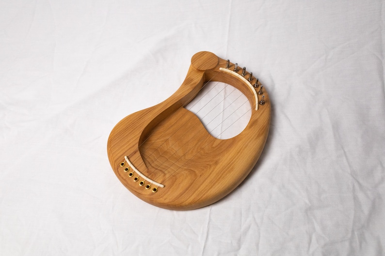 May include: A wooden lyre with a natural wood finish and a light brown color. The lyre has a curved shape and a soundboard with strings.