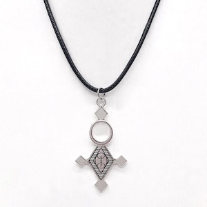 May include: Silver-toned pendant necklace with a black cord. The pendant features a geometric design with a central oval and a cross-like shape. The pendant has a detailed pattern and is suspended from a black cord.
