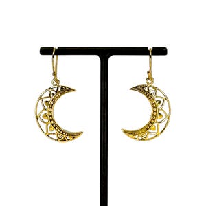 May include: A pair of gold crescent moon earrings with intricate filigree designs. The earrings are hanging from a black earring stand.