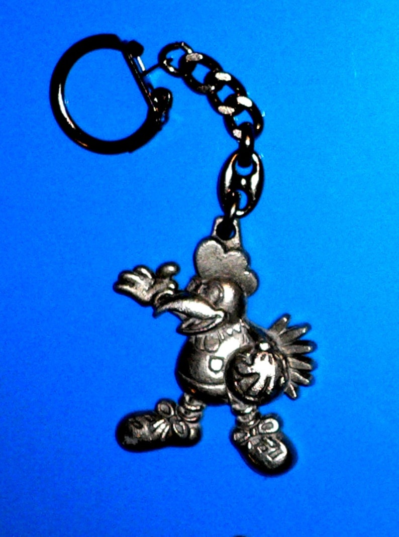 Puede incluir: Un llavero plateado con un gallo de dibujos animados sosteniendo una pelota de baloncesto. El gallo lleva una camiseta con un n&uacute;mero. El llavero tiene un anillo y una cadena de metal negro.