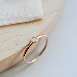 May include: A dainty gold ring featuring a small, round opal gemstone. The ring is simple and elegant, ideal for everyday wear.