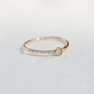 May include: A delicate gold ring with a small, round, white gemstone.