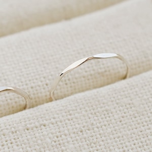 May include: Two silver rings with a hammered texture, displayed in a white fabric ring box.