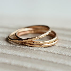 May include: Three gold hammered stacking rings. The rings are thin and delicate, and they are stacked on top of each other.