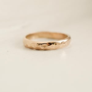 May include: A simple gold band ring with a hammered texture.