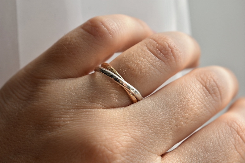 May include: A silver and gold intertwined ring with a hammered texture.