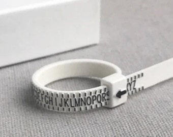 May include: White plastic ring sizer with a black arrow and letters A through Z printed on it.