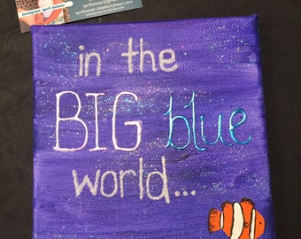 May include: A purple canvas painting with glitter embedded in the paint. The painting says "in the BIG blue world..." in white paint. A cartoon orange and white clownfish is painted in the bottom right corner.