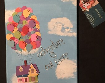 May include: A blue canvas painting with a house and balloons. The house is yellow with a purple roof and pink trim. The balloons are red, yellow, green, blue, and purple. The text "adventure is out there" is written in silver glitter on the canvas.