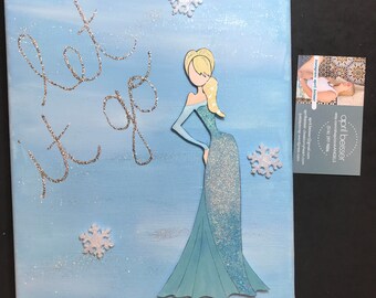 May include: A blue canvas painting with the words "let it go" written in silver glitter. A cutout of a blue sparkly dress with a blonde woman's head is on the canvas. There are white snowflakes scattered on the canvas.