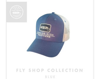 May include: Blue and white mesh trucker hat with a white logo that says "Fishing with Feathers" and a white feather graphic. The hat is part of the Fly Shop Collection.