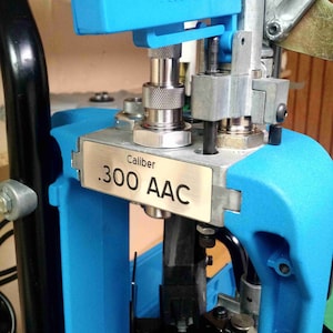 May include: A blue reloading press with a silver plate that reads "Caliber .300 AAC".