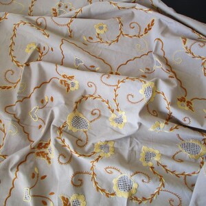 May include: A white tablecloth with brown and yellow embroidered floral designs. The tablecloth is made of a soft, lightweight fabric and has a delicate, feminine feel.