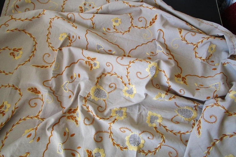 May include: A white tablecloth with brown and yellow embroidered floral designs. The tablecloth is made of a soft, lightweight fabric and has a delicate, feminine feel.