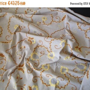 May include: A white tablecloth with embroidered floral designs in brown and yellow. The tablecloth is made of a soft, lightweight fabric and has a delicate, vintage feel.
