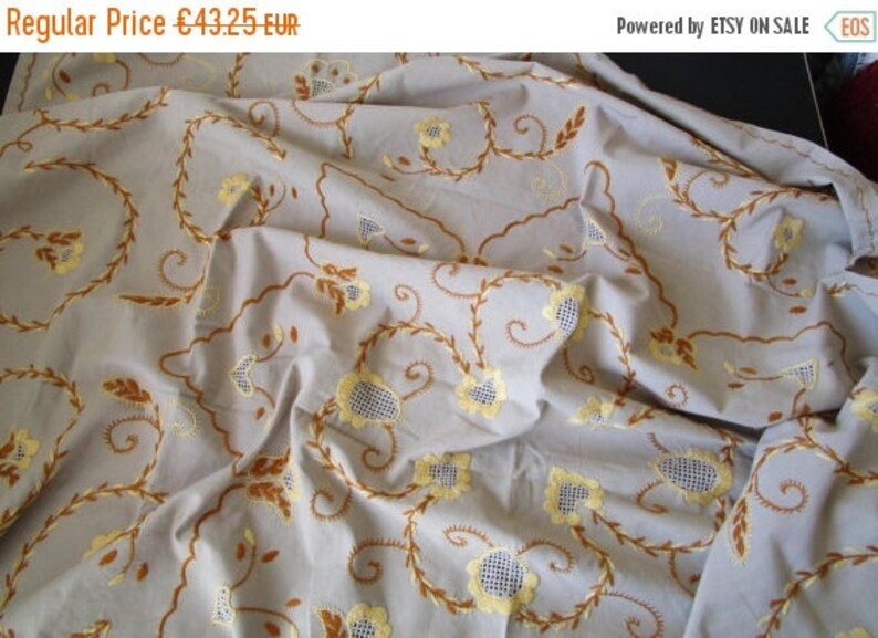 May include: A white tablecloth with embroidered floral designs in brown and yellow. The tablecloth is made of a soft, lightweight fabric and has a delicate, vintage feel.