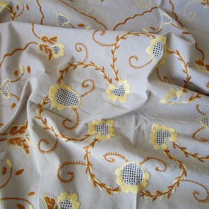 May include: A white tablecloth with embroidered yellow flowers and brown vines. The tablecloth is made of a soft, lightweight fabric and has a delicate, feminine design.