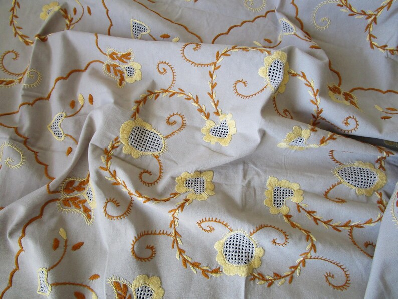 May include: A white tablecloth with embroidered yellow flowers and brown vines. The tablecloth is made of a soft, lightweight fabric and has a delicate, feminine design.