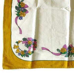 May include: A white tablecloth with a gold border and floral designs. The flowers are pink, purple, and yellow with green leaves. The tablecloth has a delicate, vintage feel.