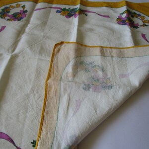 May include: A white tablecloth with a yellow border and floral designs. The tablecloth is folded in half, revealing the underside with a similar floral design.