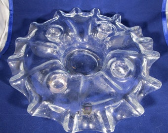 May include: Clear glass bowl with a starburst design. The bowl has a central well and several circular indentations around the rim. The rim has a scalloped, star-like shape. A small label is visible on the side of the bowl.
