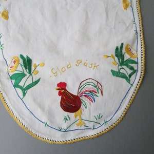 May include: White oval tablecloth with a yellow crocheted border. The tablecloth is embroidered with a rooster, flowers, and the text "Glad P&aring;sk" in yellow thread.