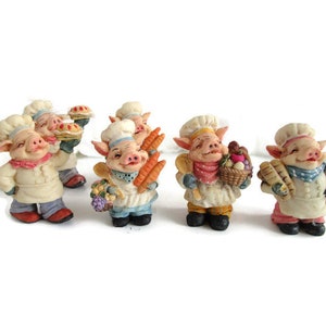 Könnte beinhalten: Eine Sammlung skurriler Schweinefiguren, die als Köche gekleidet sind. Jedes Schwein trägt eine Kochmütze und eine Schürze und hält verschiedene Lebensmittel wie Kuchen, Karotten und Brot. Die Figuren haben ein cartoonartiges Design mit lächelnden Gesichtern und farbenfrohen Akzenten.