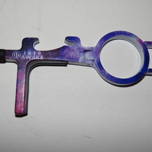 May include: A purple and blue galaxy-printed multi-tool with a stylus, bottle opener, and a loop for attaching to a keyring. The tool is labelled "IG19 AWAKE".