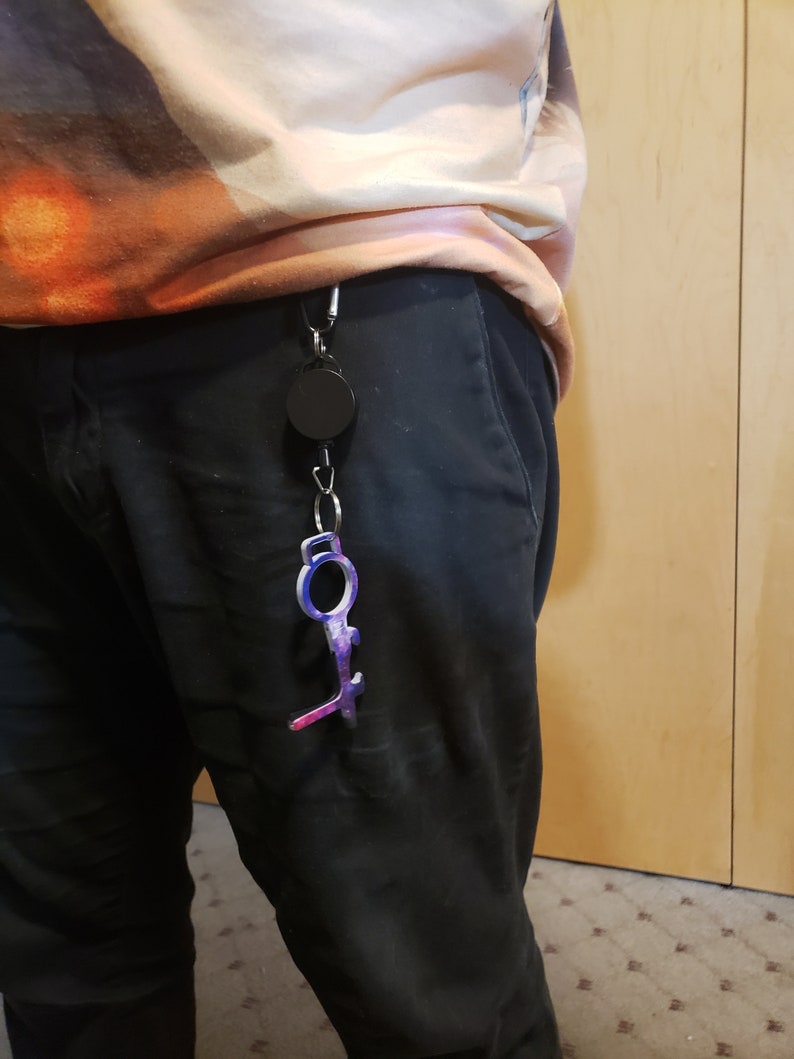 May include: A black retractable keychain with a purple and blue key-shaped tool attached. The tool has a loop at the top and a pointed end.