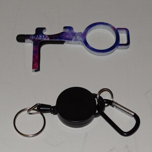 May include: A galaxy-print door opener tool with a stylus tip and bottle opener. It is attached to a black retractable key chain with a silver ring and a carabiner.