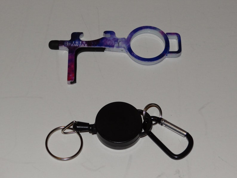 May include: A galaxy-print door opener tool with a stylus tip and bottle opener. It is attached to a black retractable key chain with a silver ring and a carabiner.
