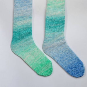 May include: Two pairs of ombre knee-high socks hanging on metal hooks. One pair is blue and green, the other is green and blue.