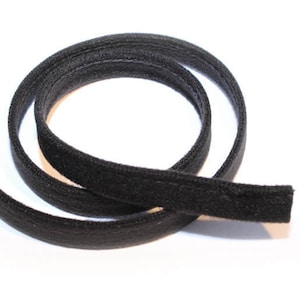 May include: A length of black piping, coiled on a white background. The piping is made of a soft, textured material and has a stitched seam running along its length. The dark color and flexible form suggest its use in sewing or crafting projects.