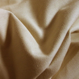 Puede incluir: Primer plano de una tela beige con un patrón de espiga. La tela es suave y tiene un brillo sutil.