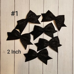 May include: Six black fabric bows with a subtle leopard print pattern. The bows are 2 inches in size and are arranged on a white wood background. #1
