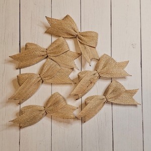 May include: Eight brown burlap bows arranged in a triangular pattern on a white wood background.